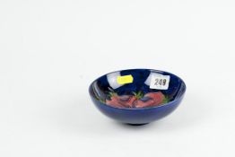 A Moorcroft circular deep blue ground pedestal dish with `Anemone` decoration, pink on one side