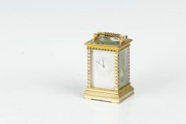 A brass encased carriage clock with bevelled panels, white dial with decorative numerals and