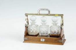 A three bottle oak and electroplated tantalus with a set of three hobnail cut whisky bottles, two