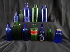 A collection of coloured glass pharmaceutical bottles and jars including a green glass bottle