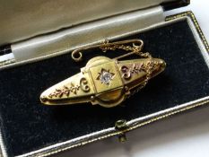 An oval Victorian fifteen carat gold pin brooch with centre star set diamond and safety chain and