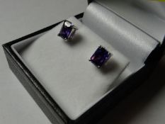 A pair of silver earrings with oblong cut purple stones.