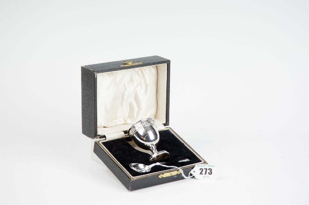 A cased spoon and egg cup set, the egg cup of plain form with a ribboned band to the top and bearing