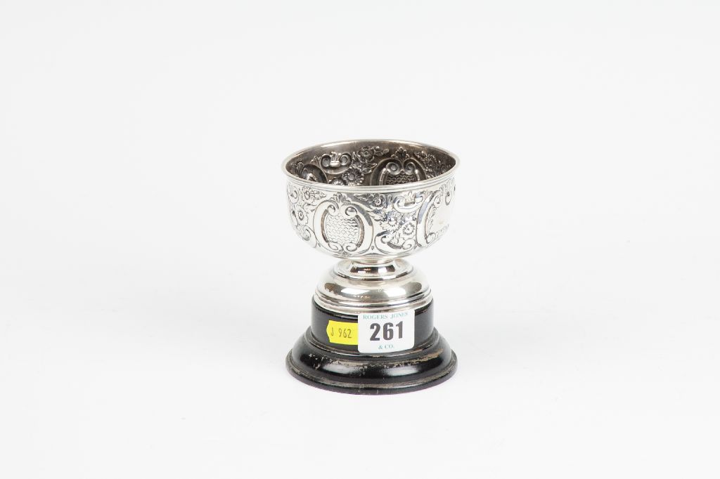 A small circular silver pedestal trophy with raised scrolled and floral decoration, 3.6 ozs,