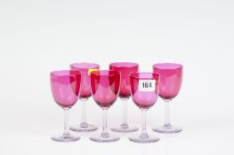 Six cranberry wine glasses with plain stems.