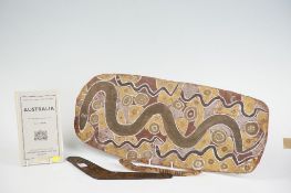An oblong Aboriginal bark painting with a serpent theme in muted maroon, pink and brown shades, 24 x