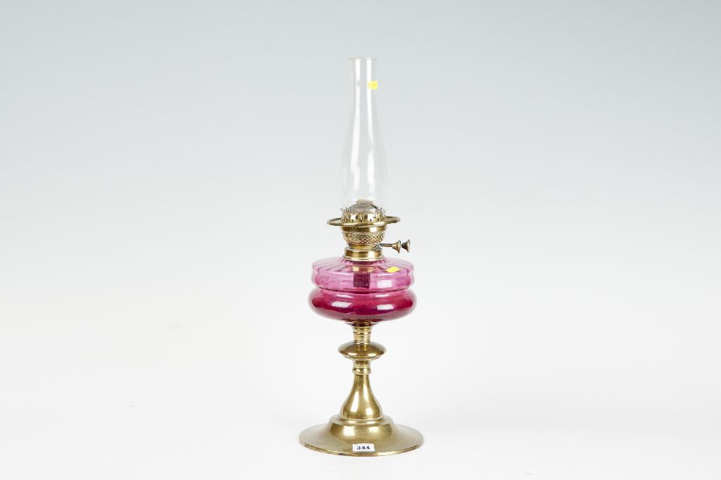 A circular based brass oil lamp with a cranberry reservoir and glass chimney, 14 ins (36 cms) high.