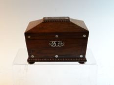 An early Victorian rosewood tea caddy of sarcophagus shape with inlaid mother-of-pearl decoration on