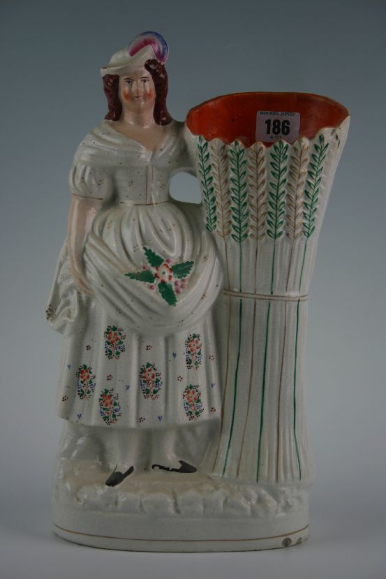 A Staffordshire figural spillholder with lady in floral dress and feathered cap and stook of corn,