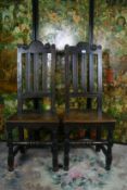A pair of 18th Century carved oak hall chairs having shaped and carved top rails with three reeded