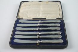 A cased set of six c.1930s silver plate butter knives. Each with leaf embossed decoration to