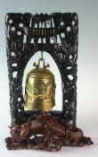 A brass Tibetan ceremonial bell hung to a carved stand with grotesque figures and mythical