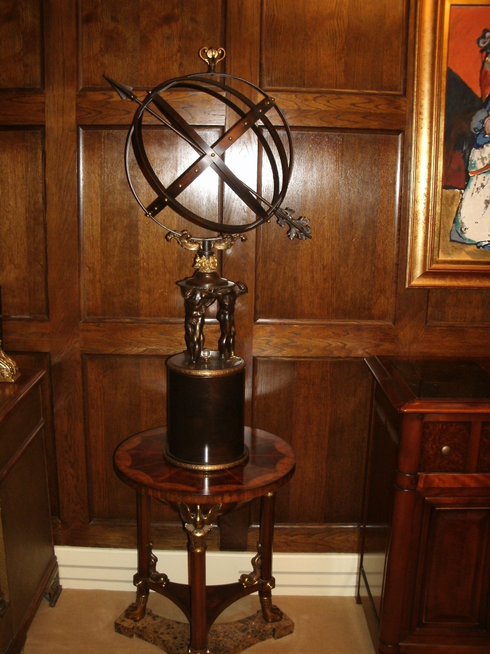 A pierced metal armillary sphere with arrow, raised on the shoulders of three male nudes, on a