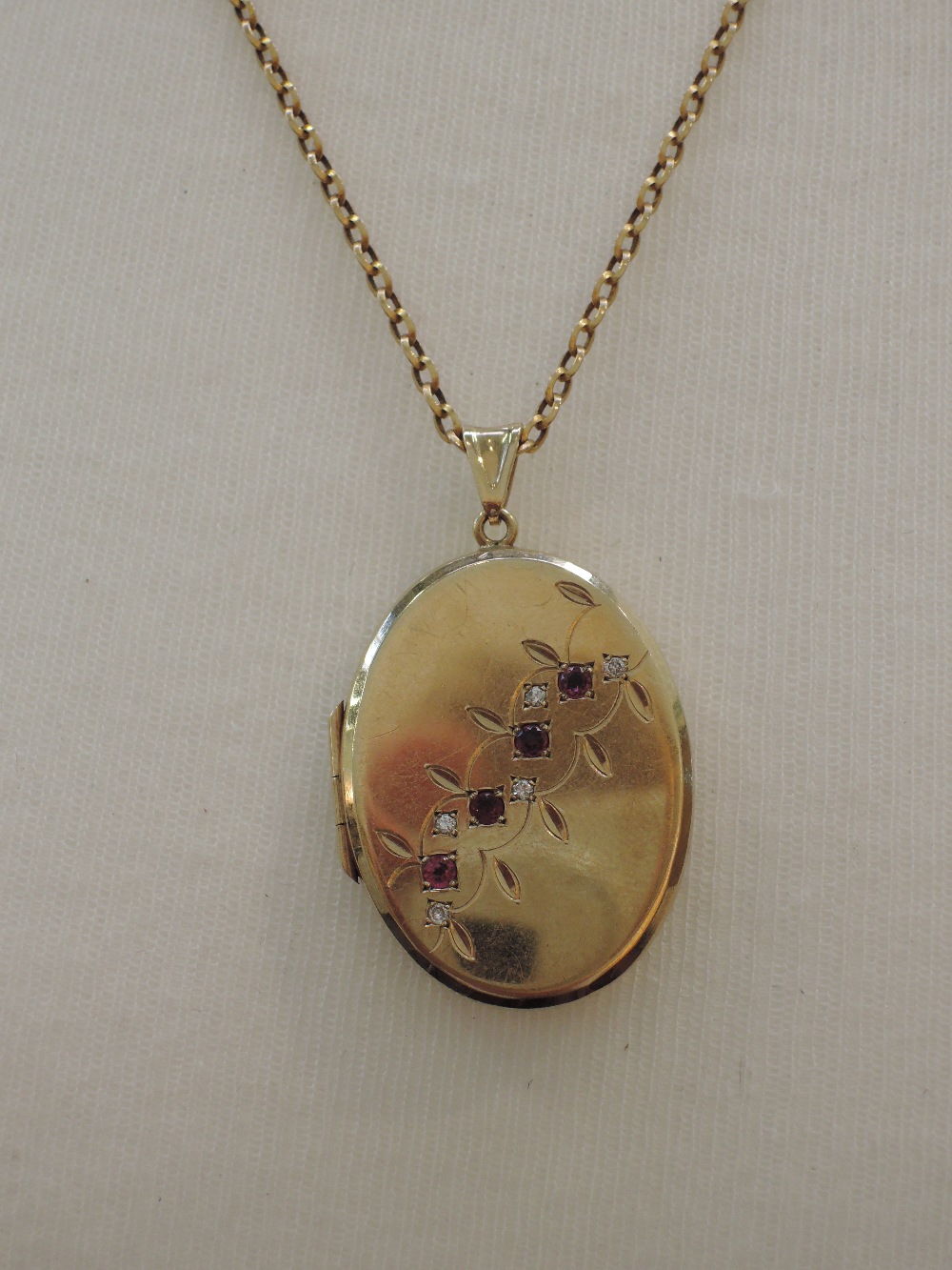 A 9ct gold oval locket having ruby and diamond foliate decoration on an open 9ct gold belcher chain