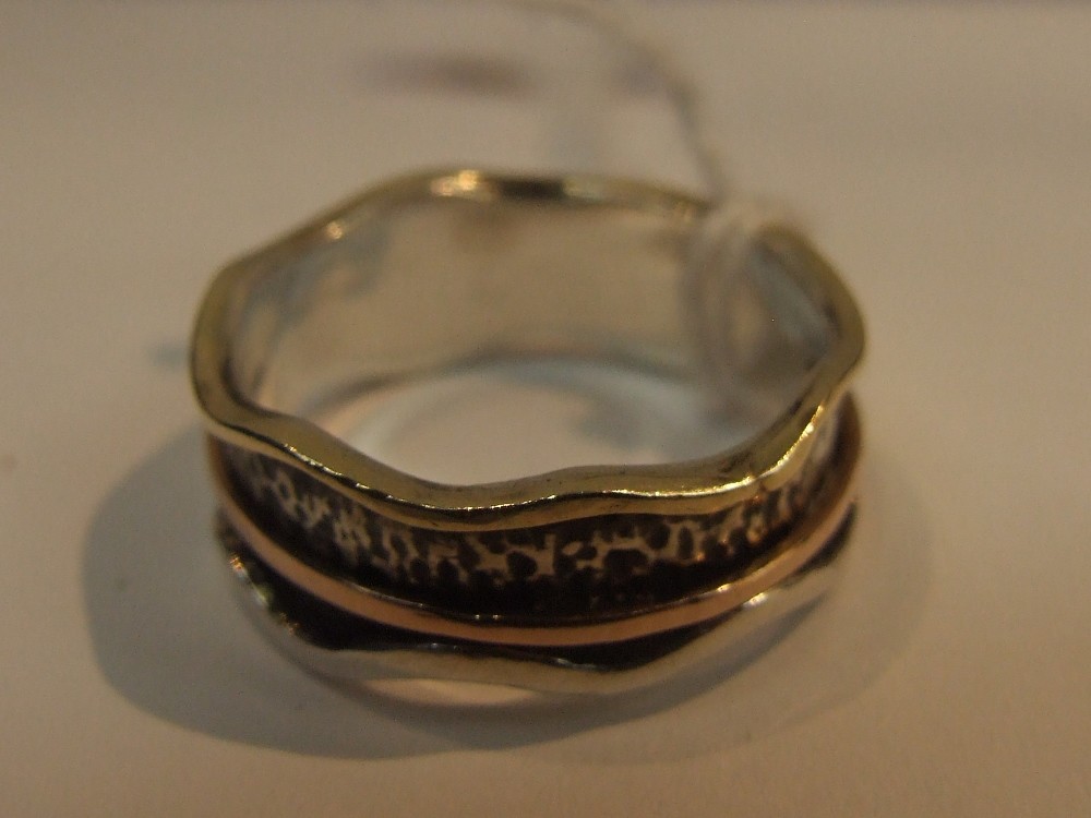 A white metal band ring stamped 925 having raised wave yellow metal decoration