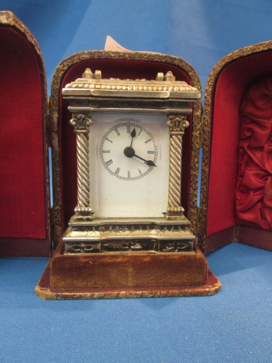 A traditional style white metal carriage clock having quartz movement in a traditional travel case