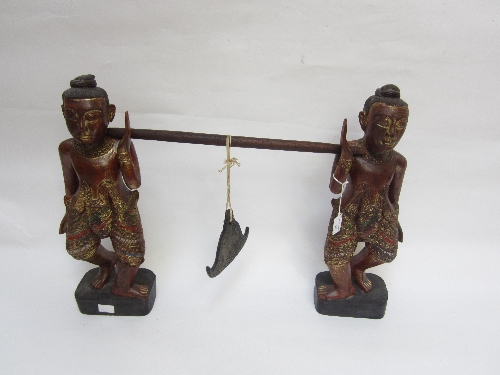 A BURMESE CARVED WOOD GONG STAND, as two men wearing gilt and glass inlaid loin cloths, carrying a