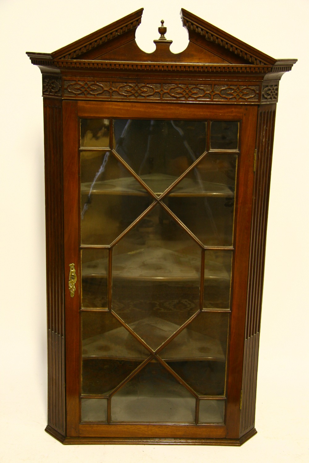 A late 18th century style mahogany hanging corner cupboard with broken-arch cornice, blind-fret