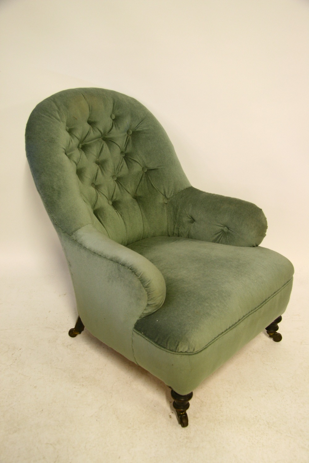 A Victorian upholstered armchair with rounded buttoned back & arms, & on short turned legs with