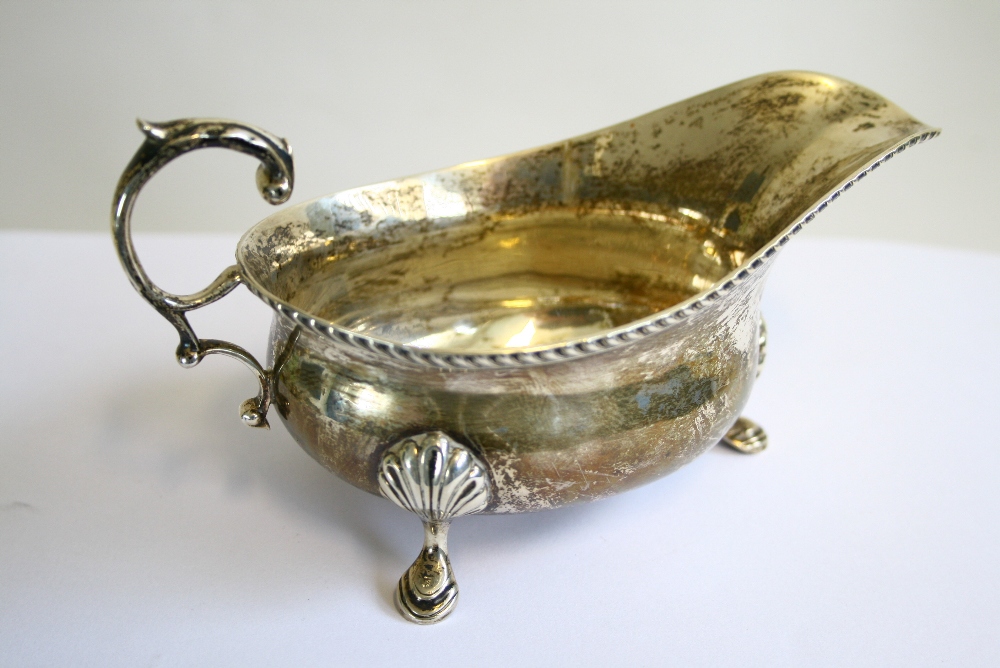 A George V oval sauce boat with gadrooned rim, open leaf-scroll handle, & on three shell-&-pad feet,