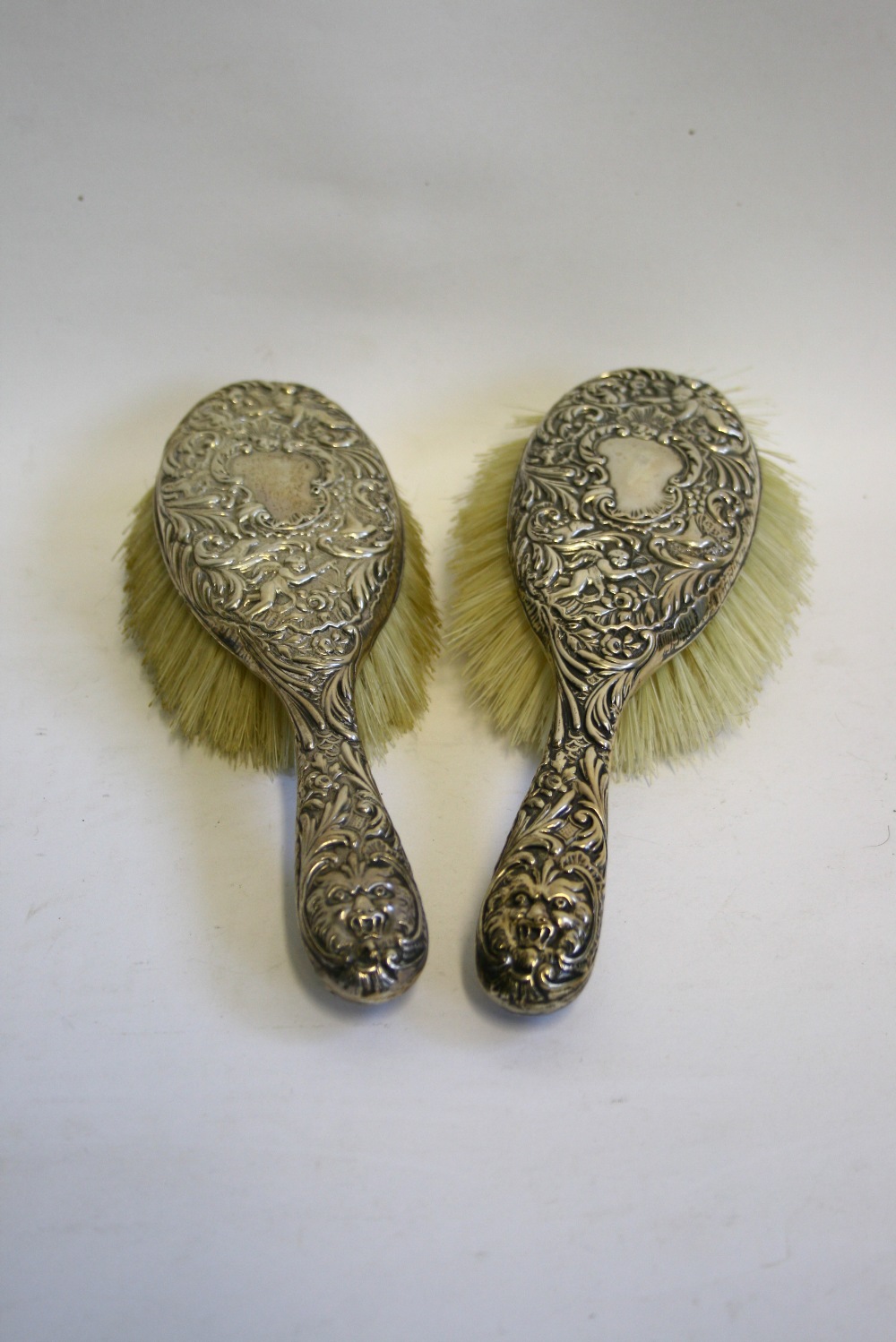 A pair of late Victorian hair brushes, the mounts embossed with cherubs, masks, flowers, & leaf-