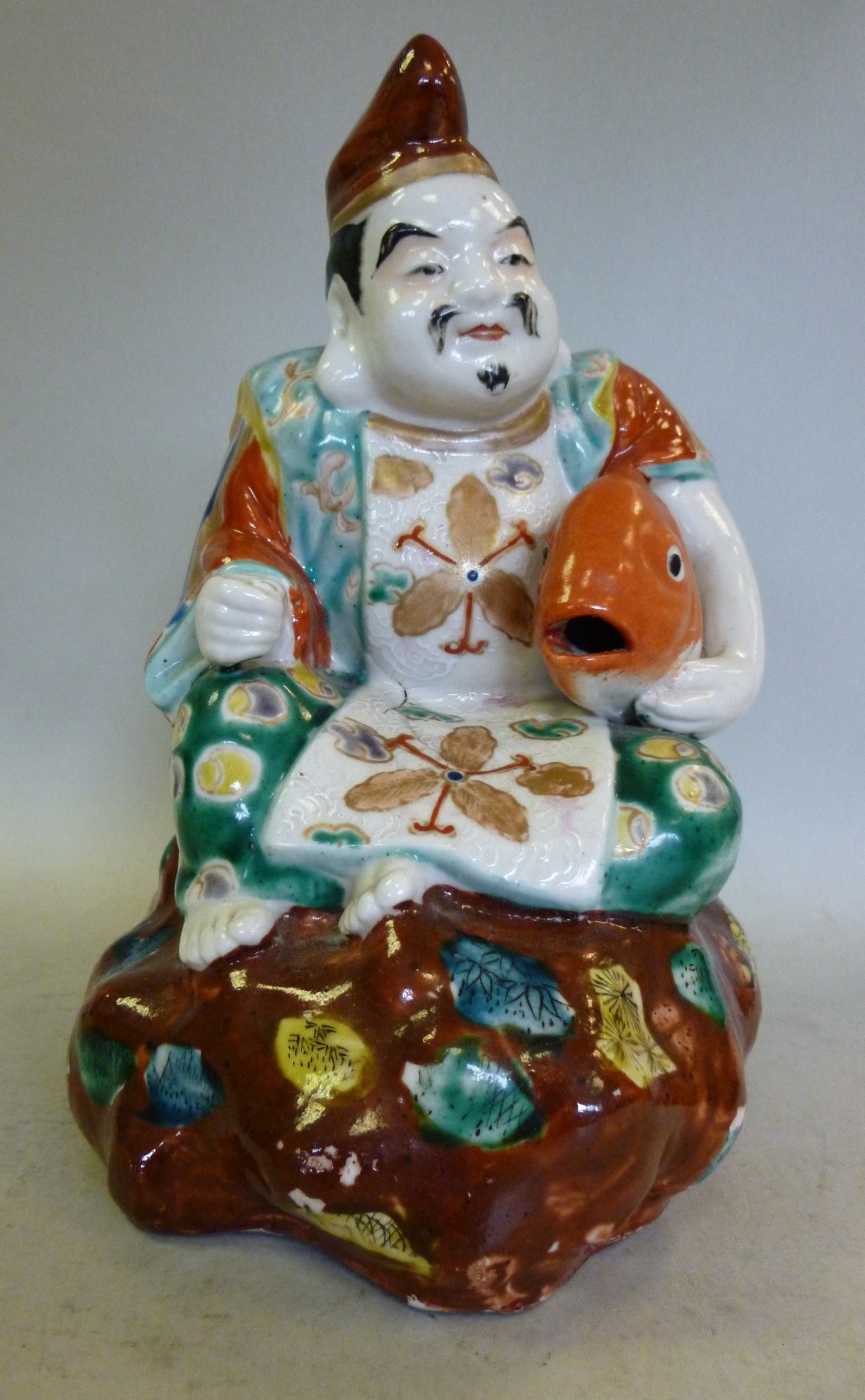 An early 20thC Japanese porcelain allegorical figure, decorated in colours, a man seated on a