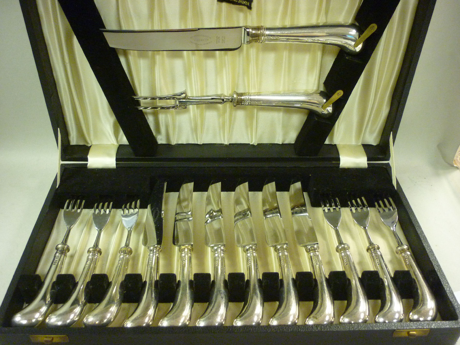 A set of six stainless steel steak knives and forks with a carving knife and fork, on cast silver