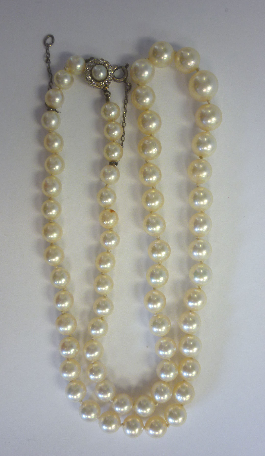 A single row, graduated cultured pearl necklet with a gold, pearl set clasp, surrounded by diamonds