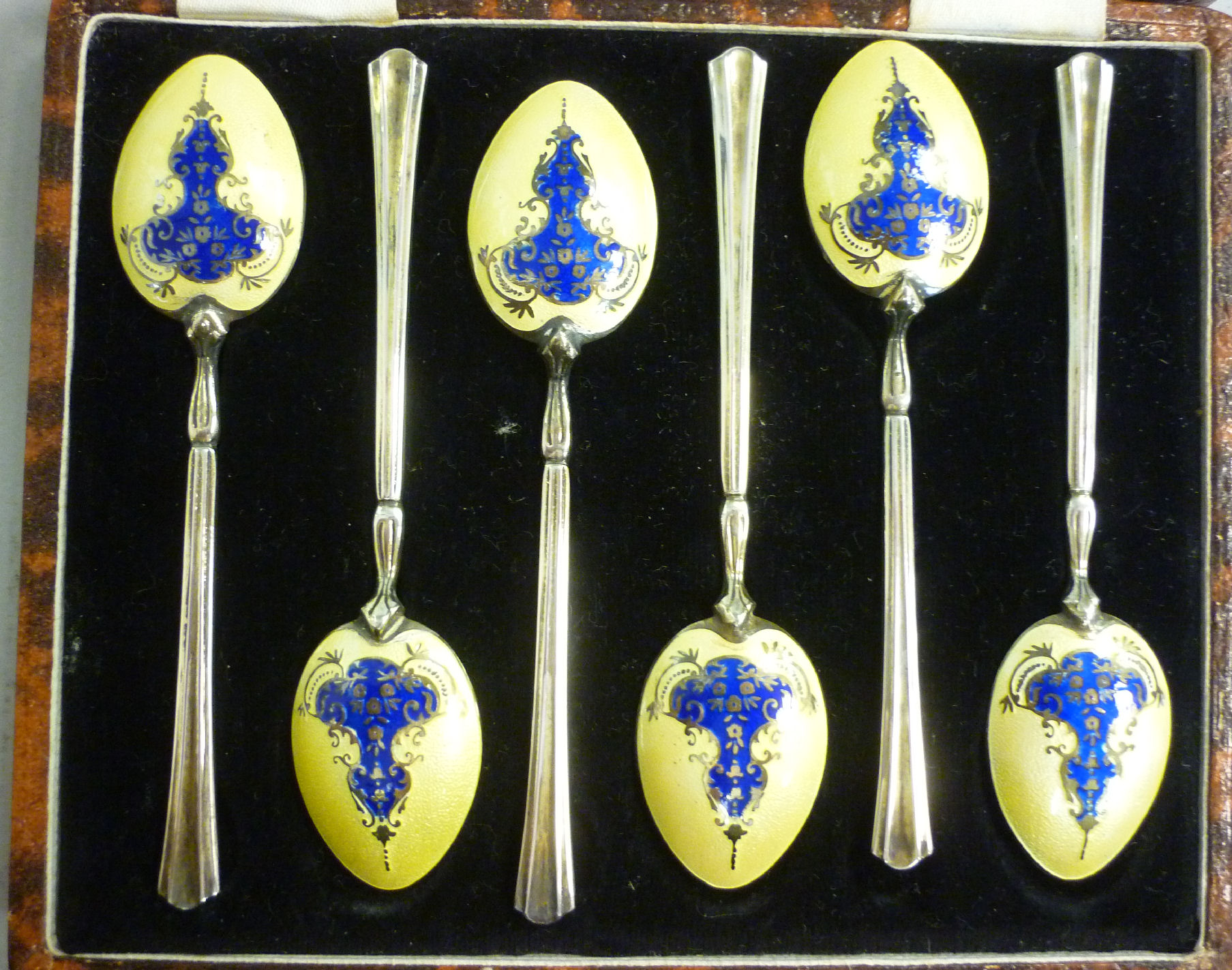 A set of six silver gilt coffee spoons with cast stems and uniformly decorated yellow and blue