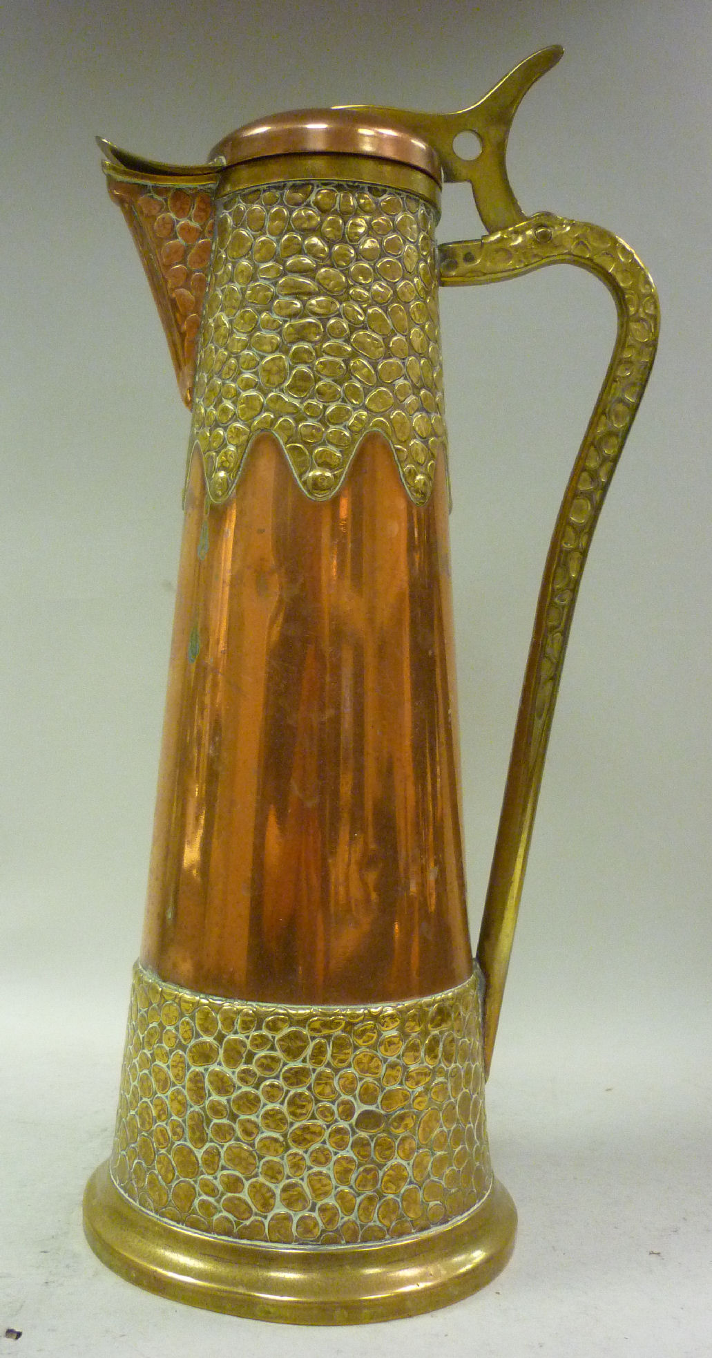 An Art Nouveau copper and brass ewer of tapered cylindrical form with hammered snakeskin effect