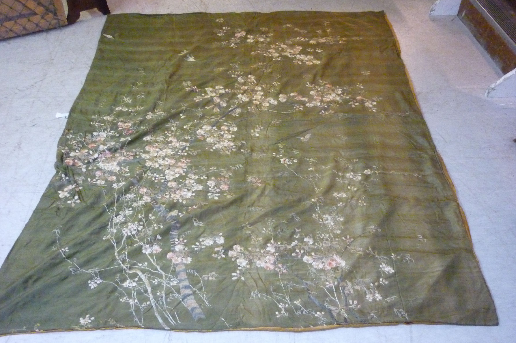 A late 19thC Chinese silk coverlet, woven with birds among flowers and foliage, on an olive green