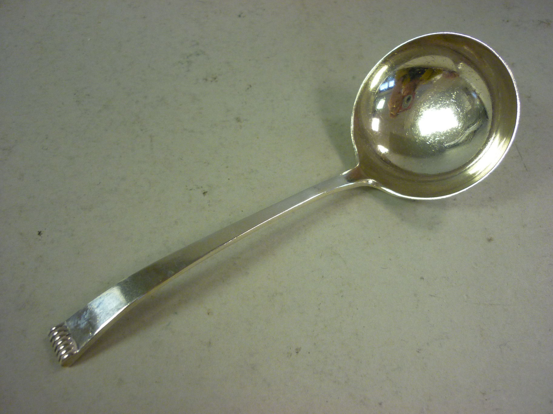 A silver sauce ladle with a circular bowl, on a tapered, flat stem and scroll cast terminal Cooper