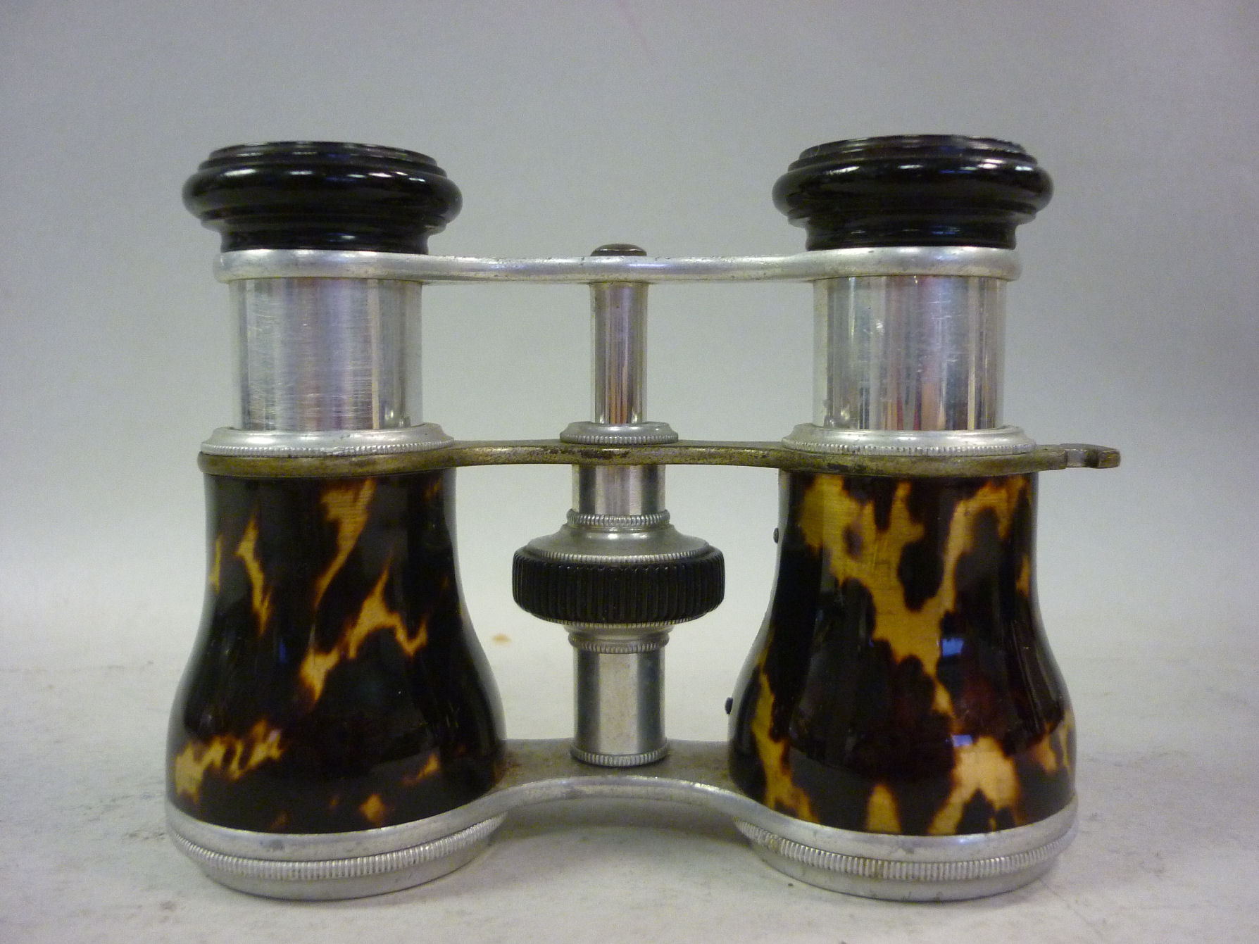 A pair of early 20thC alloy framed opera glasses, the barrels clad in simulated tortoiseshell
