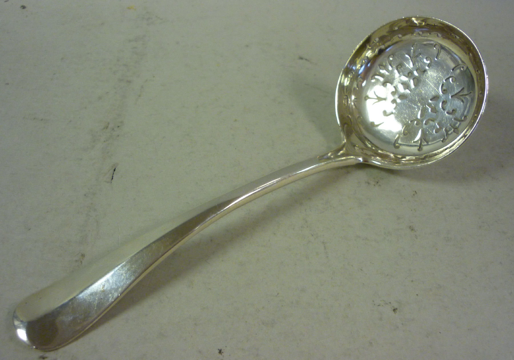 An Edwardian silver Hanoverian, rattail pattern sifter spoon with a shallow, decoratively pierced