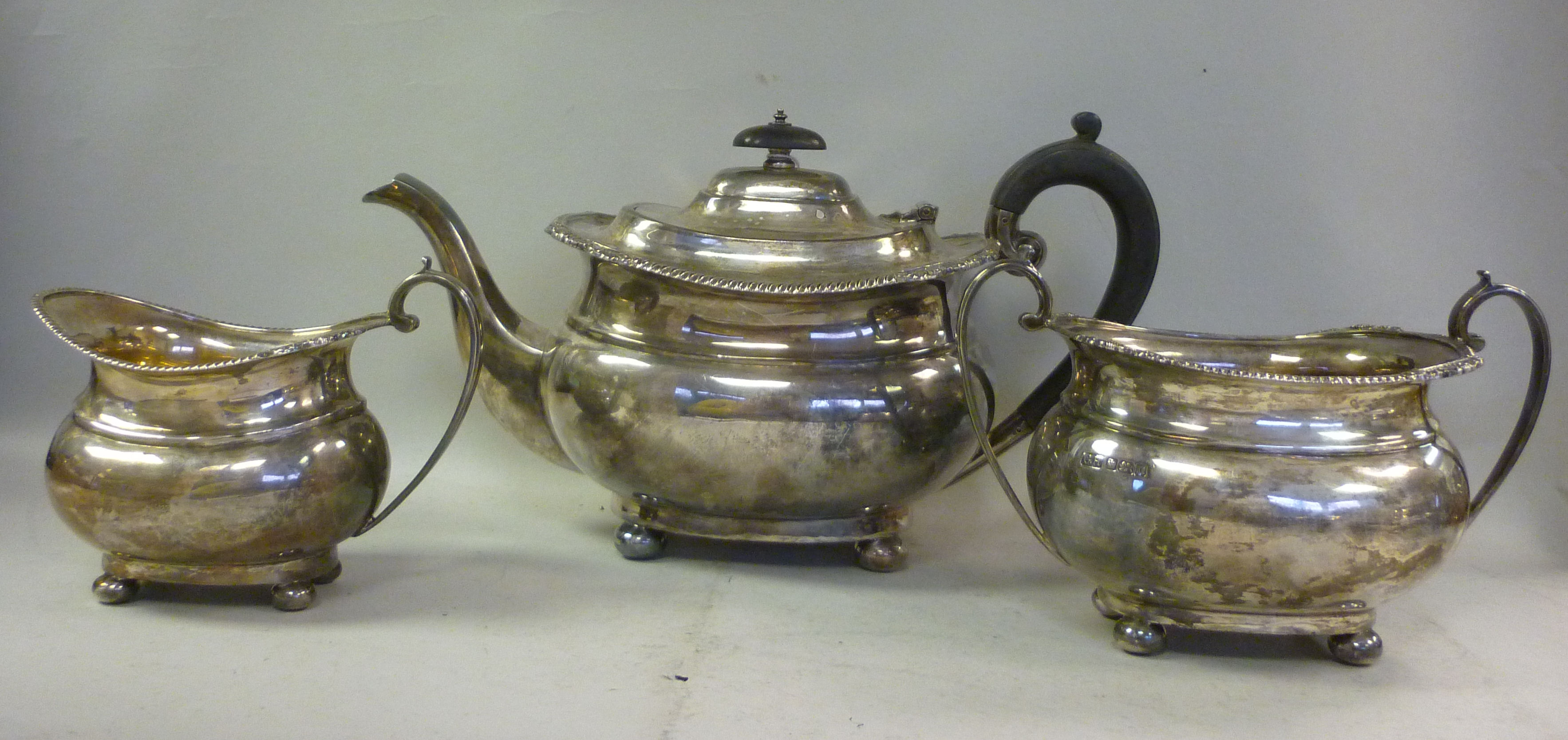 An Edwardian three piece silver tea set of oval, ogee form with flared, gadrooned and shell cast