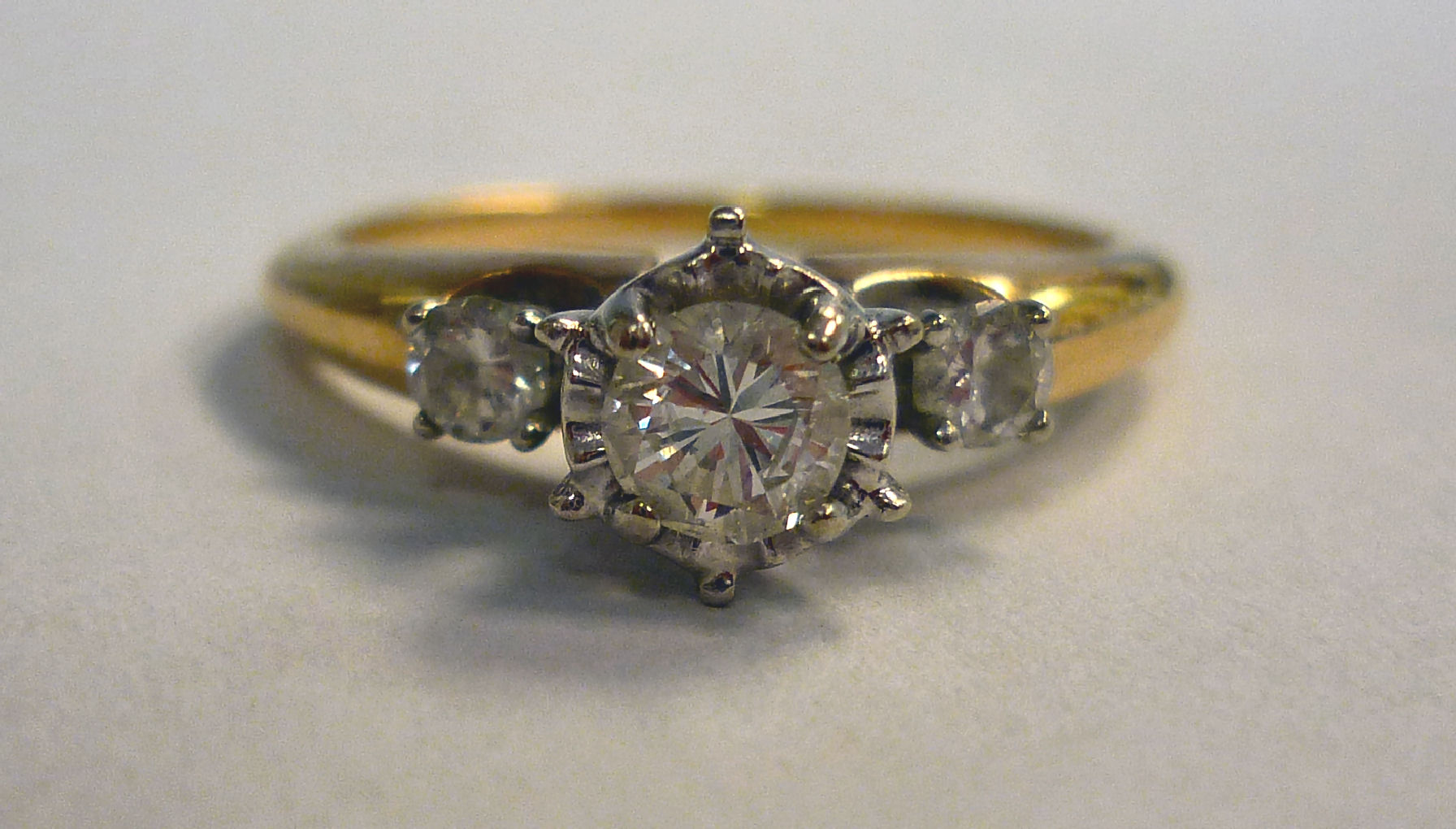 A 14ct gold ring with an illusion set diamond, between diamond shoulders