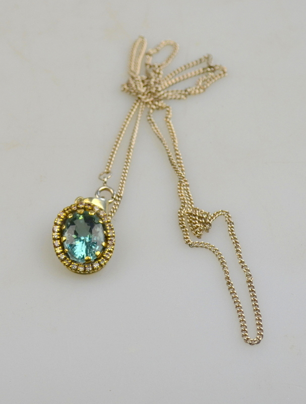 An oval aquamarine pendant with diamond surround, yellow and white metal set, on chain Condition