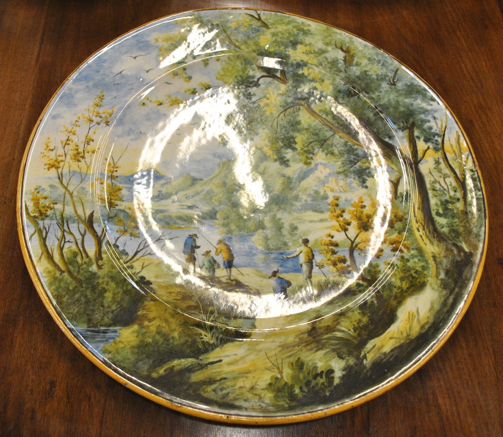 A large circular Italian majolica plaque painted with men fishing in a mountainous wooded landscape,