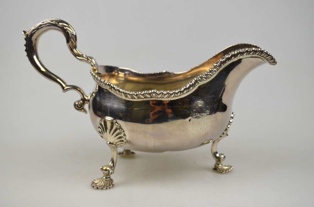 An early George III sauce boat with gadrooned rim and foliate-capped scroll handle, on three