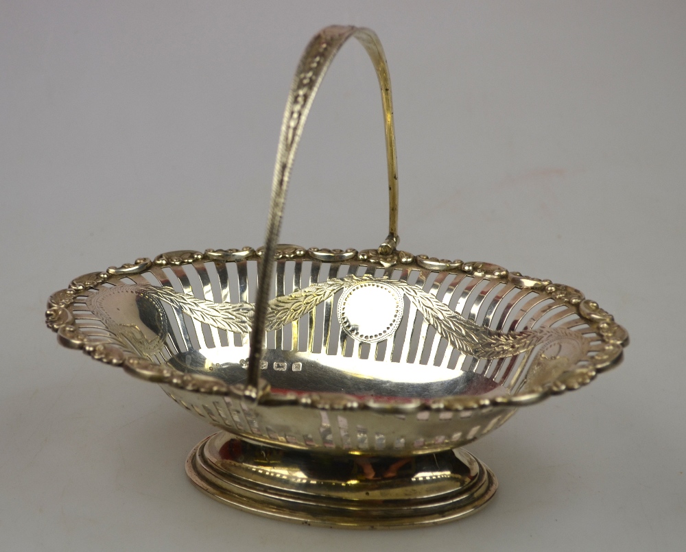 An Edwardian pierced silver oval sweetmeat basket with chased hinged handle and scroll rim, on