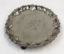 A late Victorian silver waiter, the edge decorated with shells and leaves on three scrolling feet,