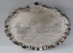 A George V silver salver with a shaped edge, on claw and ball feet, the centre engraved with an