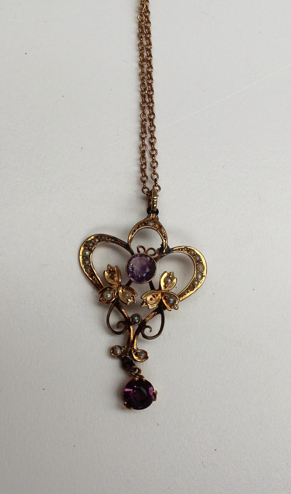 An amethyst and seed pearl pendant of scrolling shape marked 9ct on a yellow metal chain marked 9ct