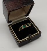 An emerald and diamond line ring, set with four oval emeralds and six diamonds to a yellow metal
