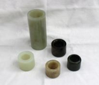 Four Chinese jade archers rings and a jade tube, 9.5cm long