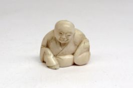 An Ivory netsuke in the form of a seated figure holding a bag, 3.5cm high.