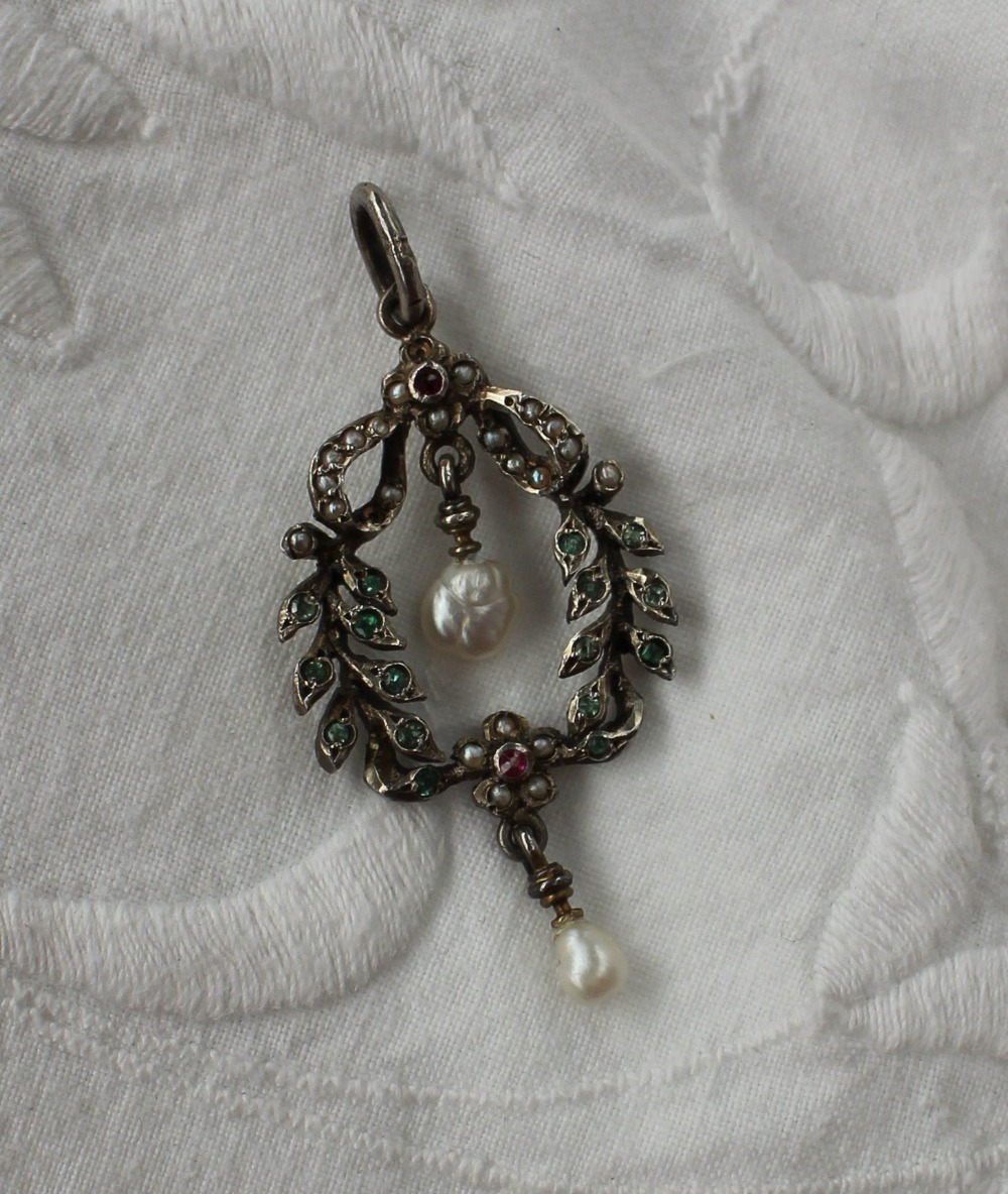 A white metal pendant set with irregular pearls, seed pearls, emeralds and rubies to a swag and