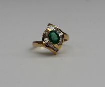 An emerald and diamond cluster ring, the central oval claw set emerald surrounded by baguette cut