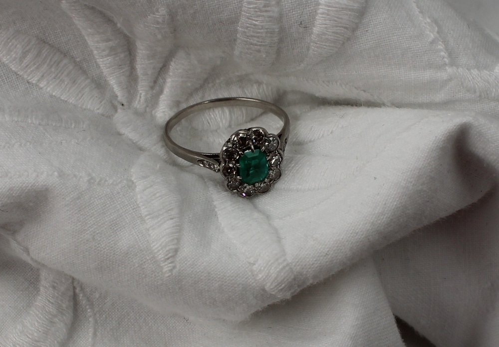 An emerald and diamond cluster ring the central oval emerald surrounded by ten old cut diamonds to
