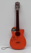 A Beatles orange plastic guitar with paper sticker roundel and facsimile signatures, 74.5cm long